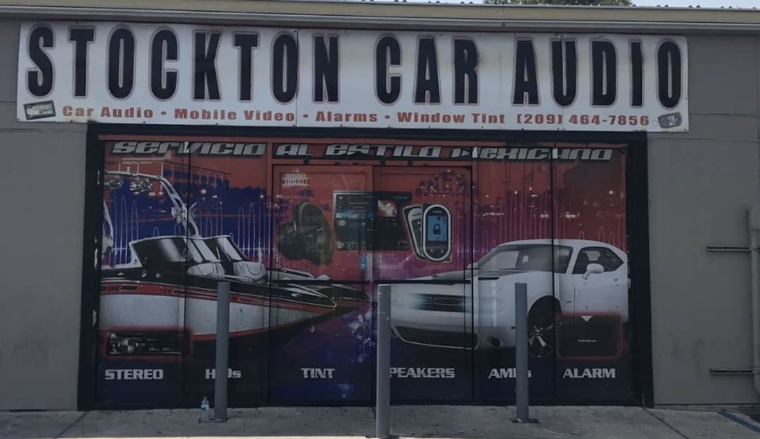 Stockton Car Audio storefront before: a dark red and purple window wrap with a Spanish headline and floating product images, service words along the sill.