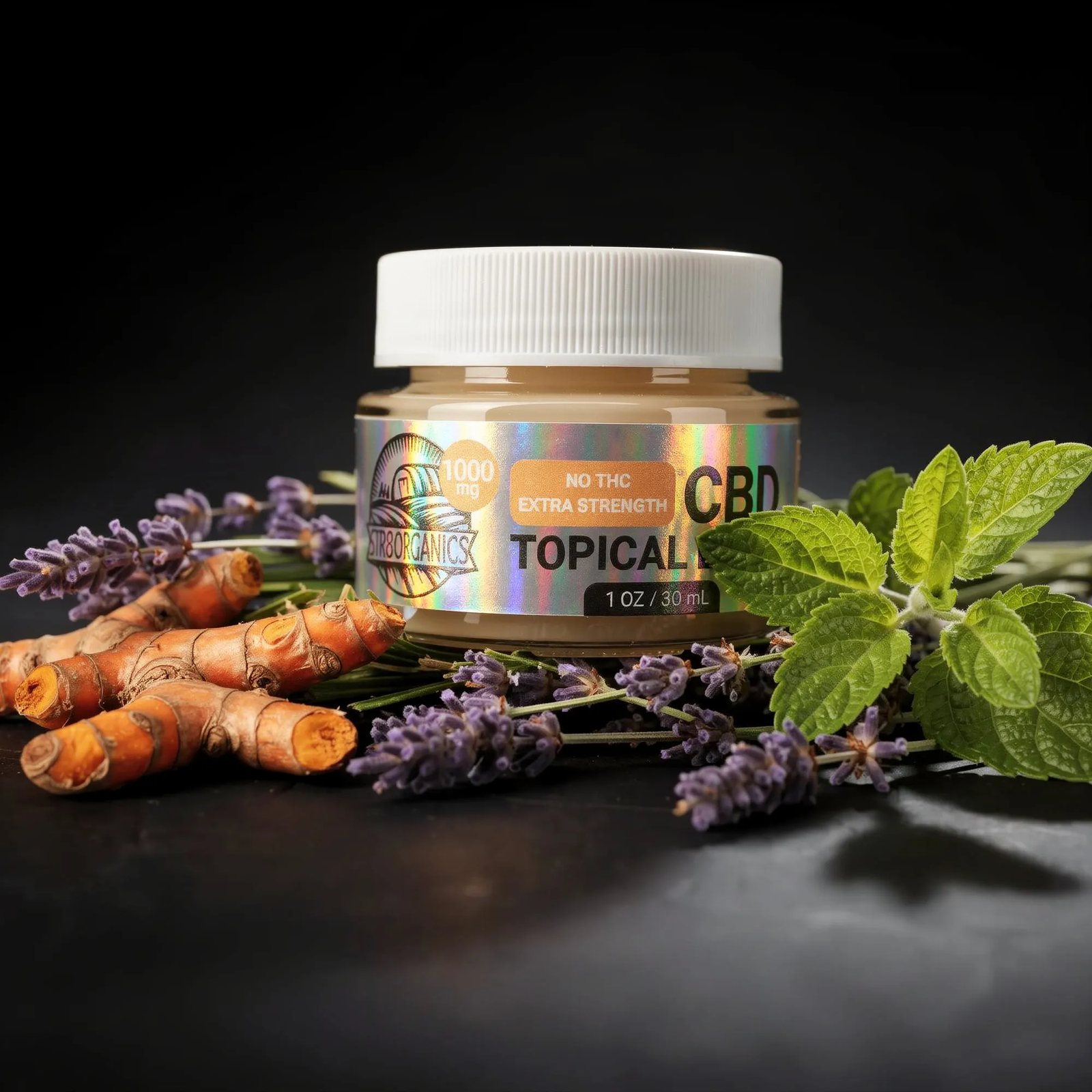 Styled shot of the holographic topical balm jar on a dark ground with lavender, turmeric root and mint arranged around it.